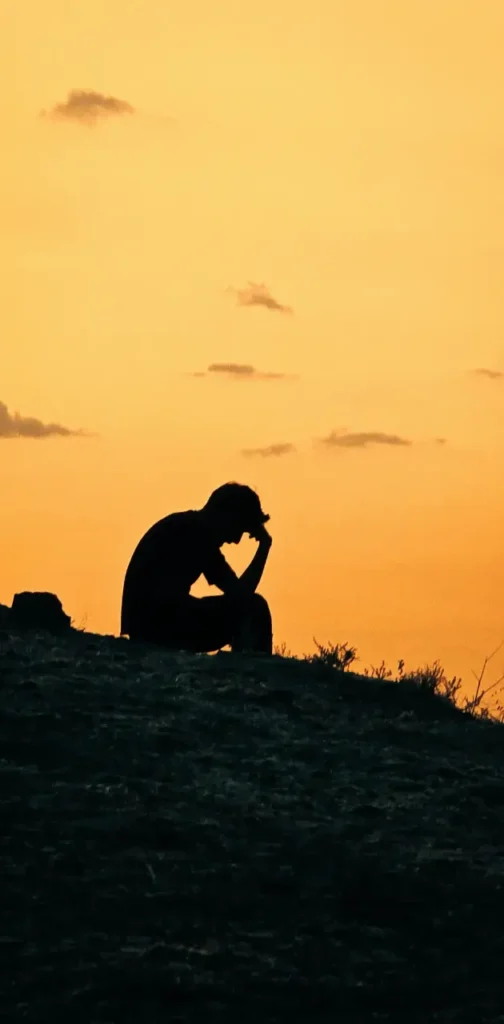 Silhouette of a man sitting in a thinking pose on a mountain, representing overthinking and repetitive thought patterns.